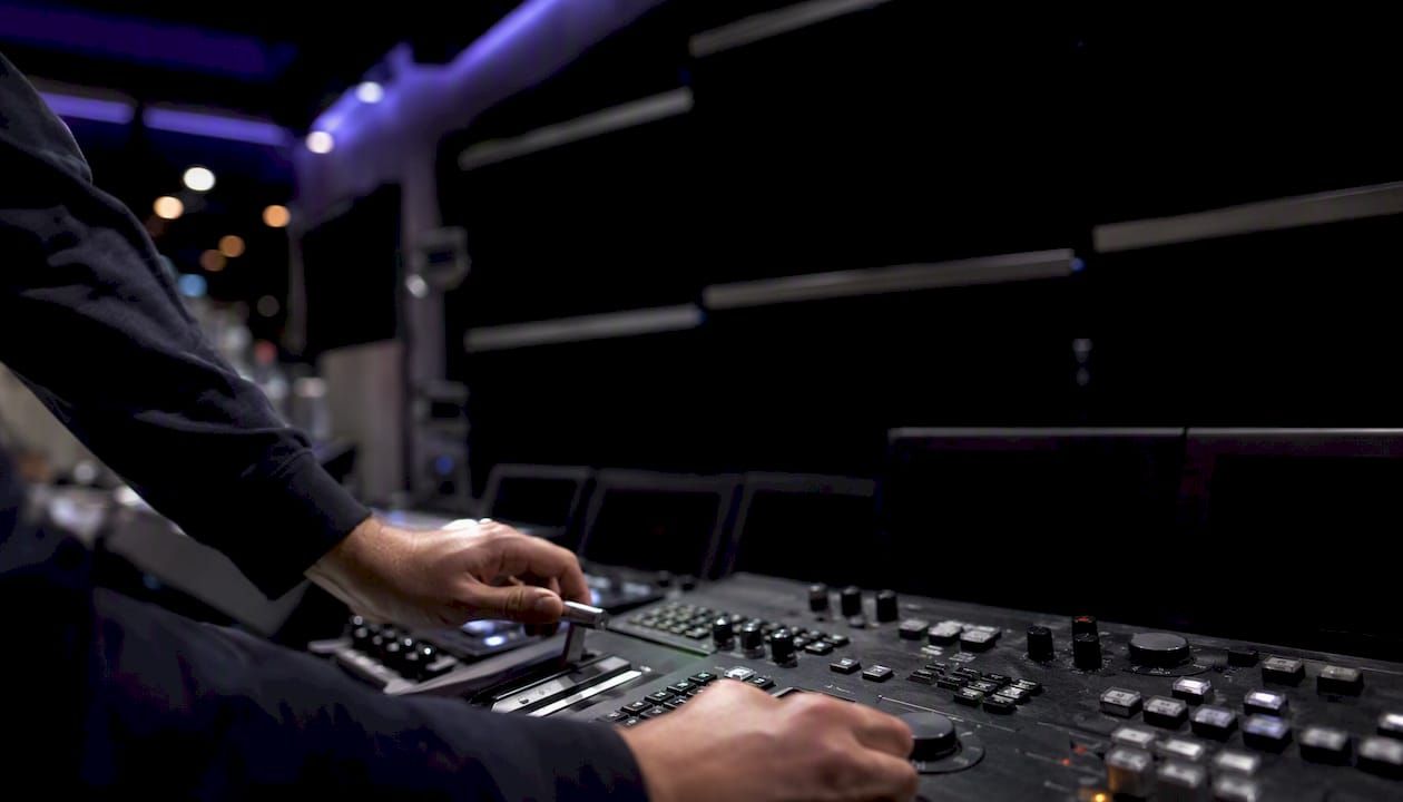 Hands adjusting the faders and knobs of a control desk in a darkened room